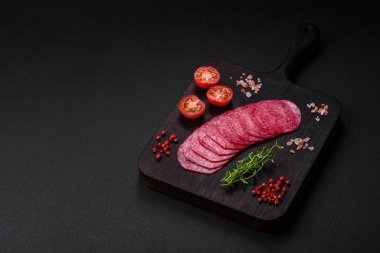 Lezzetli tütsülenmiş salam sosisi, tuz, baharat ve otlar koyu beton arka planda dilimler halinde kesilmiş.