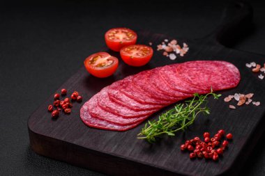 Lezzetli tütsülenmiş salam sosisi, tuz, baharat ve otlar koyu beton arka planda dilimler halinde kesilmiş.