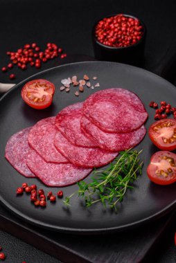 Lezzetli tütsülenmiş salam sosisi, tuz, baharat ve otlar koyu beton arka planda dilimler halinde kesilmiş.