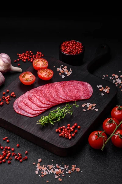 stock image Delicious smoked salami sausage with salt, spices and herbs cut into slices on a dark concrete background