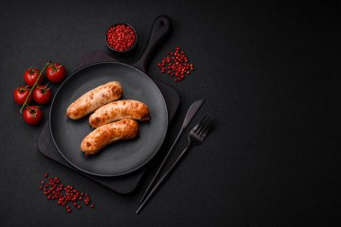 Lezzetli ızgara sosis, tuz, baharat ve otlar seramik tabakta koyu beton arka planda.