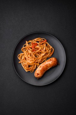 Lezzetli ızgara sosis, makarna, tuz, baharat ve otlu erişte, koyu beton bir arka planda seramik tabakta.