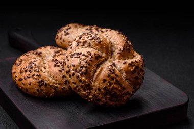 Lezzetli taze pişmiş çıtır çörekler ya da koyu beton arka planda susam tohumlu Kayzer rulosu.