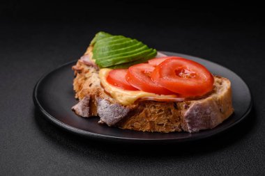 Lezzetli ızgara tost, jambon, peynir, domates ve koyu beton arka planda tuzlu, baharatlı ve otlu avokado.