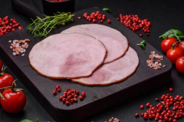 Lezzetli taze jambon, tuz, baharat ve otlarla kesilmiş koyu beton arka planda yuvarlak dilimler halinde.