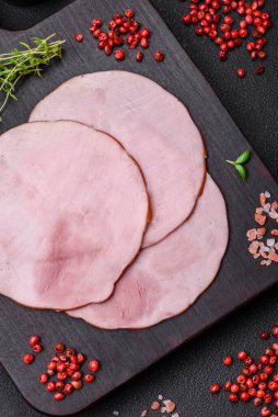 Lezzetli taze jambon, tuz, baharat ve otlarla kesilmiş koyu beton arka planda yuvarlak dilimler halinde.