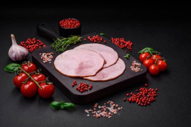 Lezzetli taze jambon, tuz, baharat ve otlarla kesilmiş koyu beton arka planda yuvarlak dilimler halinde.