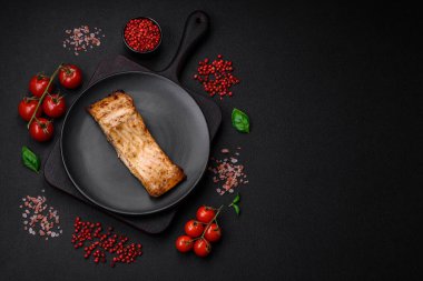 Tuzlu, baharatlı ve otlu lezzetli bir balık dilimi seramik bir tabakta koyu beton arka planda.