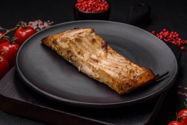 Tuzlu, baharatlı ve otlu lezzetli bir balık dilimi seramik bir tabakta koyu beton arka planda.