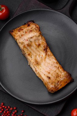 Tuzlu, baharatlı ve otlu lezzetli bir balık dilimi seramik bir tabakta koyu beton arka planda.