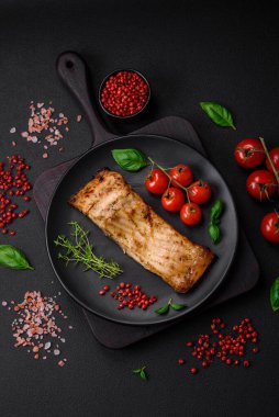 Tuzlu, baharatlı ve otlu lezzetli bir balık dilimi seramik bir tabakta koyu beton arka planda.