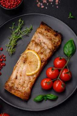 Tuzlu, baharatlı ve otlu lezzetli bir balık dilimi seramik bir tabakta koyu beton arka planda.