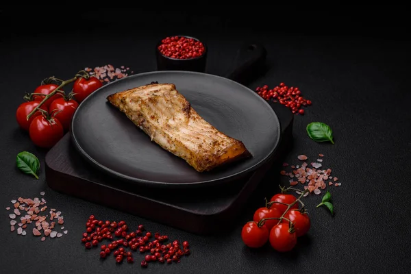 stock image Slice of delicious baked fish with salt, spices and herbs on a ceramic plate on a dark concrete background