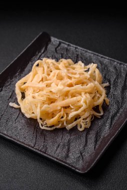 Koyu beton arka planda seramik bir tabakta tuz ve baharat içeren lezzetli kurutulmuş mürekkep balığı.