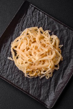 Koyu beton arka planda seramik bir tabakta tuz ve baharat içeren lezzetli kurutulmuş mürekkep balığı.