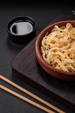 Koyu beton arka planda seramik bir tabakta tuz ve baharat içeren lezzetli kurutulmuş mürekkep balığı.