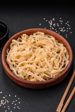 Koyu beton arka planda seramik bir tabakta tuz ve baharat içeren lezzetli kurutulmuş mürekkep balığı.