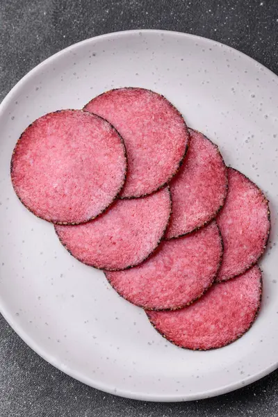 stock image Delicious smoked salami sausage with salt, pepper, spices and herbs on a textured concrete background