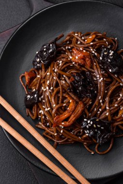 Lezzetli taze karabuğday eriştesi ya da mantarlı udon, biber ve diğer sebzeler, baharatlar ve otlar koyu beton arka planda.