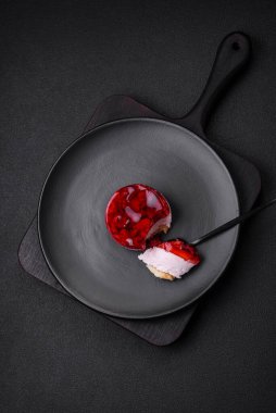 Lezzetli taze peynirli kek, böğürtlenli ve kırmızı renkli jöle, koyu beton arka planda.