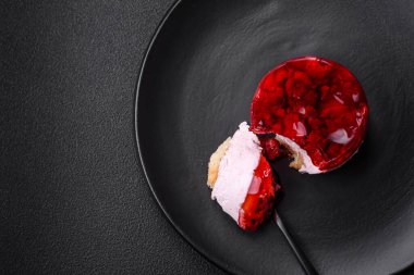 Lezzetli taze peynirli kek, böğürtlenli ve kırmızı renkli jöle, koyu beton arka planda.