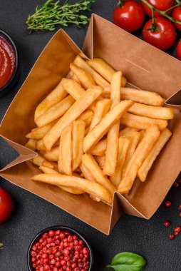 Lezzetli çıtır patates kızartması. Koyu beton bir arka planda karton bir kutuda tuz ve baharatla.