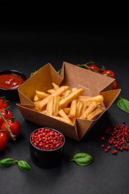 Lezzetli çıtır patates kızartması. Koyu beton bir arka planda karton bir kutuda tuz ve baharatla.