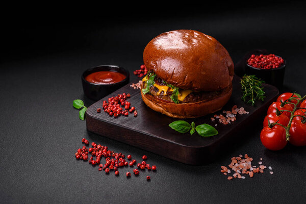 Burger with juicy beef cutlet, cheese, tomatoes, salt, spices and herbs on a dark concrete background