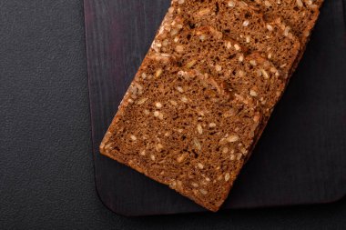 Tohumları ve tahılları koyu beton arka planda dilimlenmiş lezzetli taze çıtır kahverengi ekmek.