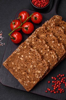 Tohumları ve tahılları koyu beton arka planda dilimlenmiş lezzetli taze çıtır kahverengi ekmek.