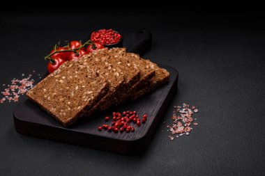 Tohumları ve tahılları koyu beton arka planda dilimlenmiş lezzetli taze çıtır kahverengi ekmek.