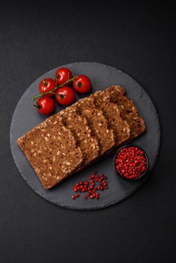 Tohumları ve tahılları koyu beton arka planda dilimlenmiş lezzetli taze çıtır kahverengi ekmek.