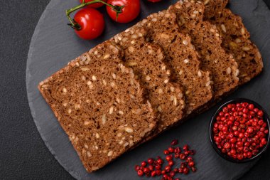 Tohumları ve tahılları koyu beton arka planda dilimlenmiş lezzetli taze çıtır kahverengi ekmek.