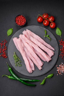 Çiğ tavuk ya da hindi filetosu koyu beton arka planda baharat ve otlarla şeritler halinde kesilmiş.