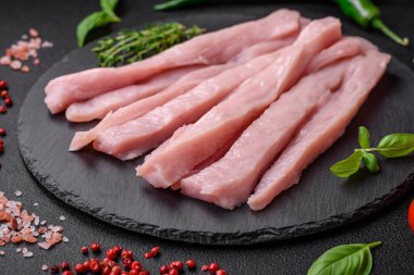 Çiğ tavuk ya da hindi filetosu koyu beton arka planda baharat ve otlarla şeritler halinde kesilmiş.