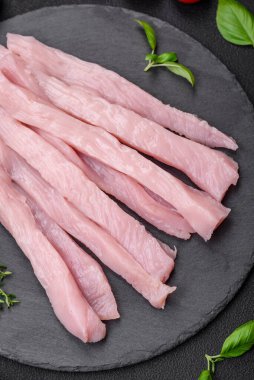 Çiğ tavuk ya da hindi filetosu koyu beton arka planda baharat ve otlarla şeritler halinde kesilmiş.