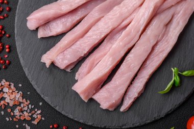 Çiğ tavuk ya da hindi filetosu koyu beton arka planda baharat ve otlarla şeritler halinde kesilmiş.