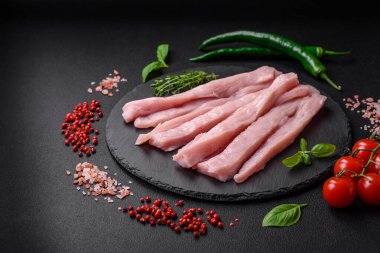 Çiğ tavuk ya da hindi filetosu koyu beton arka planda baharat ve otlarla şeritler halinde kesilmiş.