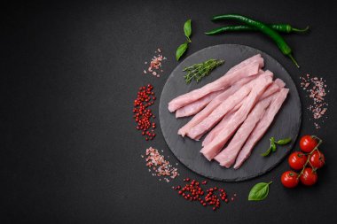 Çiğ tavuk ya da hindi filetosu koyu beton arka planda baharat ve otlarla şeritler halinde kesilmiş.