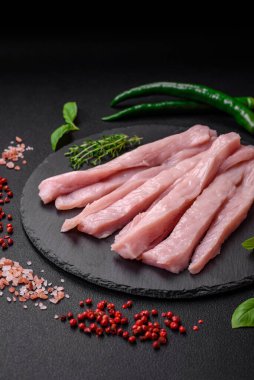 Çiğ tavuk ya da hindi filetosu koyu beton arka planda baharat ve otlarla şeritler halinde kesilmiş.