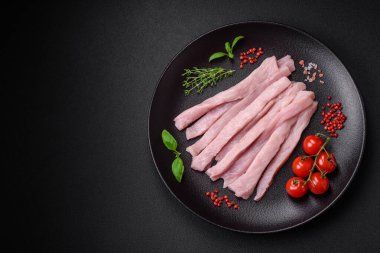 Çiğ tavuk ya da hindi filetosu koyu beton arka planda baharat ve otlarla şeritler halinde kesilmiş.