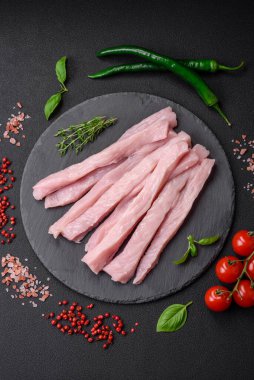 Çiğ tavuk ya da hindi filetosu koyu beton arka planda baharat ve otlarla şeritler halinde kesilmiş.