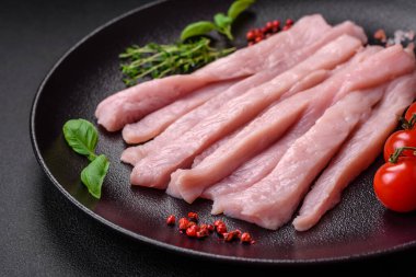 Çiğ tavuk ya da hindi filetosu koyu beton arka planda baharat ve otlarla şeritler halinde kesilmiş.