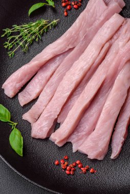 Çiğ tavuk ya da hindi filetosu koyu beton arka planda baharat ve otlarla şeritler halinde kesilmiş.