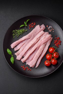 Çiğ tavuk ya da hindi filetosu koyu beton arka planda baharat ve otlarla şeritler halinde kesilmiş.