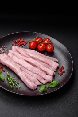 Çiğ tavuk ya da hindi filetosu koyu beton arka planda baharat ve otlarla şeritler halinde kesilmiş.