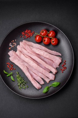 Çiğ tavuk ya da hindi filetosu koyu beton arka planda baharat ve otlarla şeritler halinde kesilmiş.