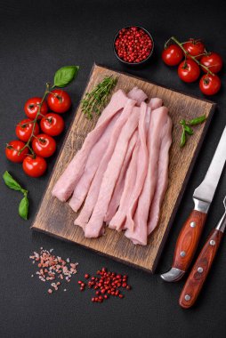 Çiğ tavuk ya da hindi filetosu koyu beton arka planda baharat ve otlarla şeritler halinde kesilmiş.