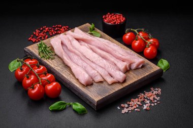 Çiğ tavuk ya da hindi filetosu koyu beton arka planda baharat ve otlarla şeritler halinde kesilmiş.