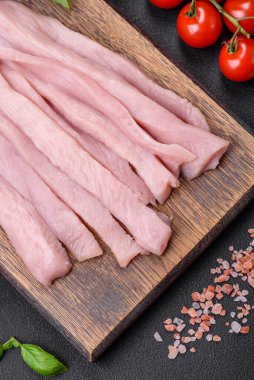 Çiğ tavuk ya da hindi filetosu koyu beton arka planda baharat ve otlarla şeritler halinde kesilmiş.